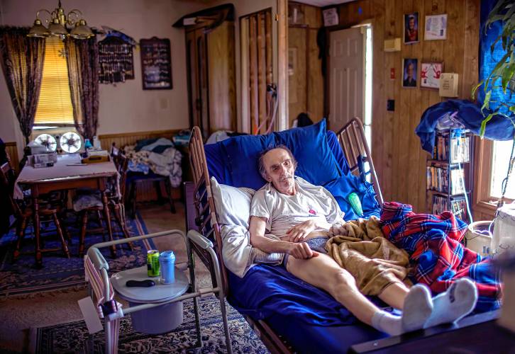 John Jones lies in the hospital bed in the living room of his Franklin house on August 9, 2023, six months after the stroke that left him without the use of his left arm.