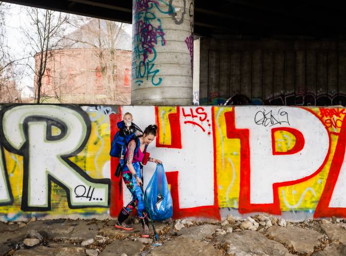 Brianna Heath cleans up debris along the railroad tracks underneath the Water Street bridge with her son, Maverick, in a backpack on Saturday. The group of citizens worked the corridor from I-93 exits 13 through 15.