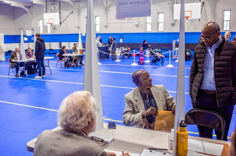 Clement Kigugu (right), the director at Overcomers, who had given him a ride to the location, helps Kayitani Ndutiye with translations as he registers to vote for the first time in the United States at the Green Street Community Center on Primary Day in New Hampshire.
