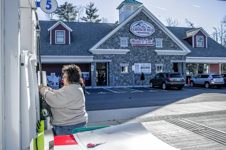 Deb Gureckis, merchandiser for the Common Man stores, puts up signage on the gas pumps in front of the new Roadside Market and Deli at the Epsom Circle on Tuesday, January 2, 2024.
