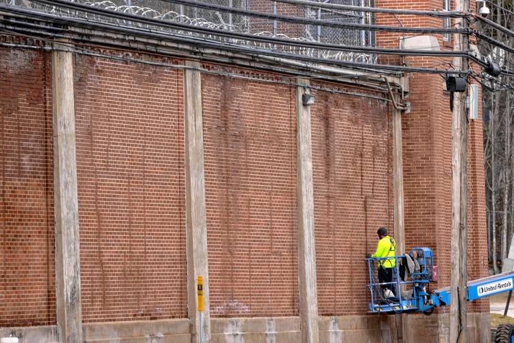 A worker uses a lift to work on the outside brick wall of the New Hampshire State Prison on North State Street on Wednesday, March 20, 2024.