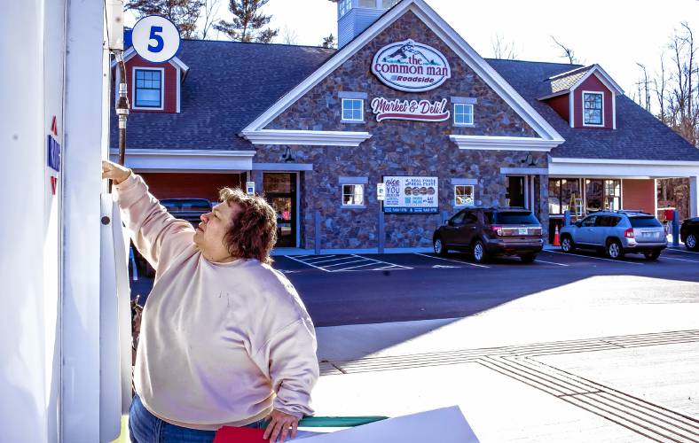 Deb Gureckis, merchandiser for the Common Man stores, puts up signage on the gas pumps in front of the new Roadside Market and Deli at the Epsom Circle on Tuesday.