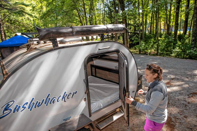 Suncook River Camp owner Kim Caprio opens the door to a small teardrop camper that holds a queen-sized mattress.