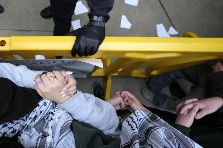 Pro-Palestinian protesters clasp their hands as a University of Chicago police officer holds onto a barricade  on May 7.
