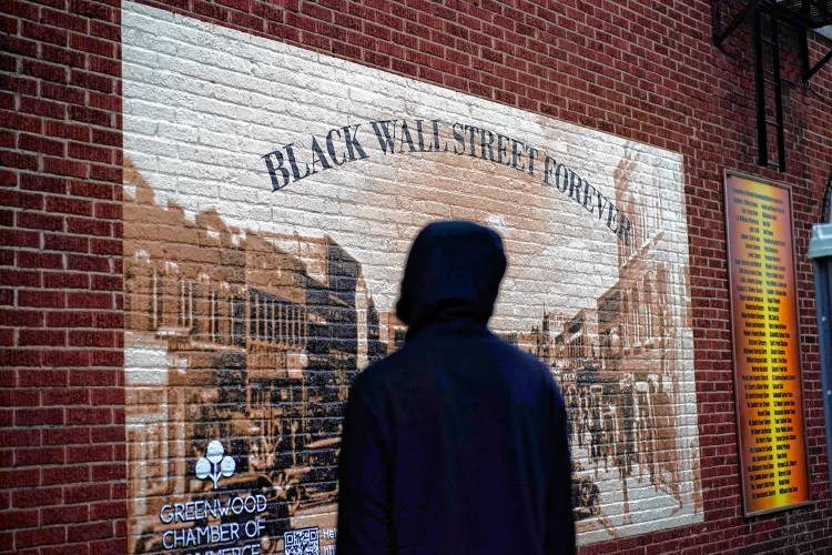 A man looks at a Black Wall Street mural in the historic Greenwood neighborhood of Tulsa, Okla., Thursday, May 27, 2021, ahead of centennial commemorations of the Tulsa Race Massacre.