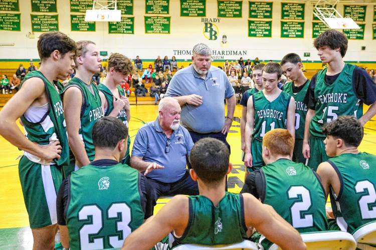 Pembroke Academy boys’ basketball head coach Mike Donnell (sitting) and assistant coach Jim Cilley (standing) speak to the team during a timeout in a game last season. The Spartans were the Division II runner-up team in 2022-23 and semifinals last season.