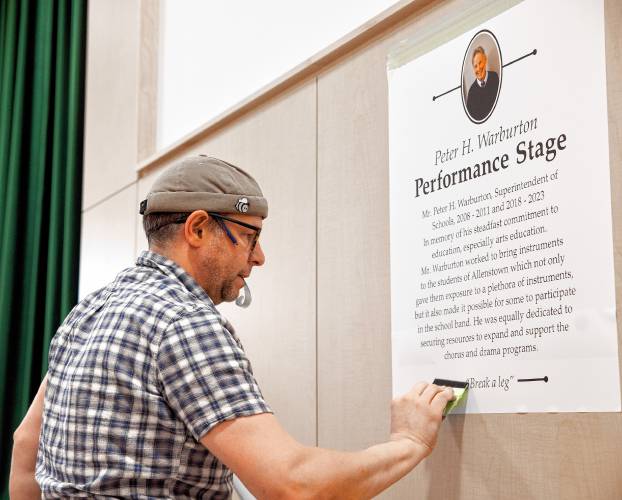 Jake Bouchard of Advantage Signs  attaches a poster in honor of former Superintendent Peter H. Warburton at the stage and gymnasium at the Allenstown Community School on Friday, May 3, 2024. Warburton died a year ago and they dedicated the stage to him.