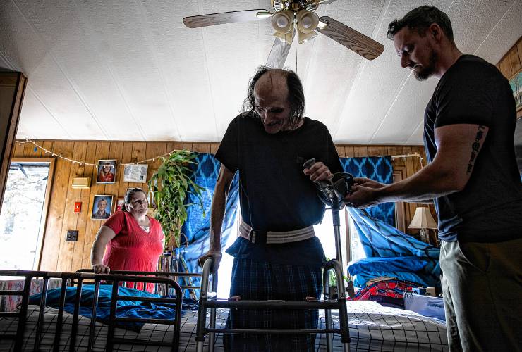John Jones starts a round of walking around using a walker his home in Franklin with the help of his physical therapist Justin Levesque on April 29, 2024 as Jessica Helfenstein looks on.