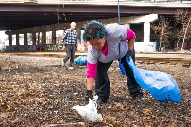 Tracey Pierce picks up debris along the tracks underneath Water Street near the Common Man on Saturday morning, April 19, 2025. A group led by Concord city councilor Jeff Foote cleaned up the area called the Concord corridor between exits 13 and 15 of I-93.